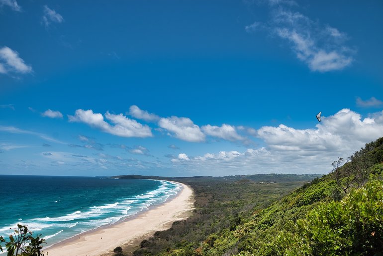 A hang-glider, on a the right-hand side, floating over Tallow Beach